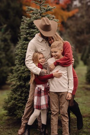A family shares joyful moments together among evergreen trees during an autumn photoshoot in warm earth-toned outfits.