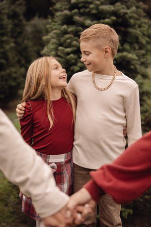 A couple in red and beige sweaters share a romantic moment while holding hands against an evergreen backdrop.