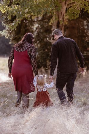 Family walking together through tall autumn grass in a park setting at sunset.