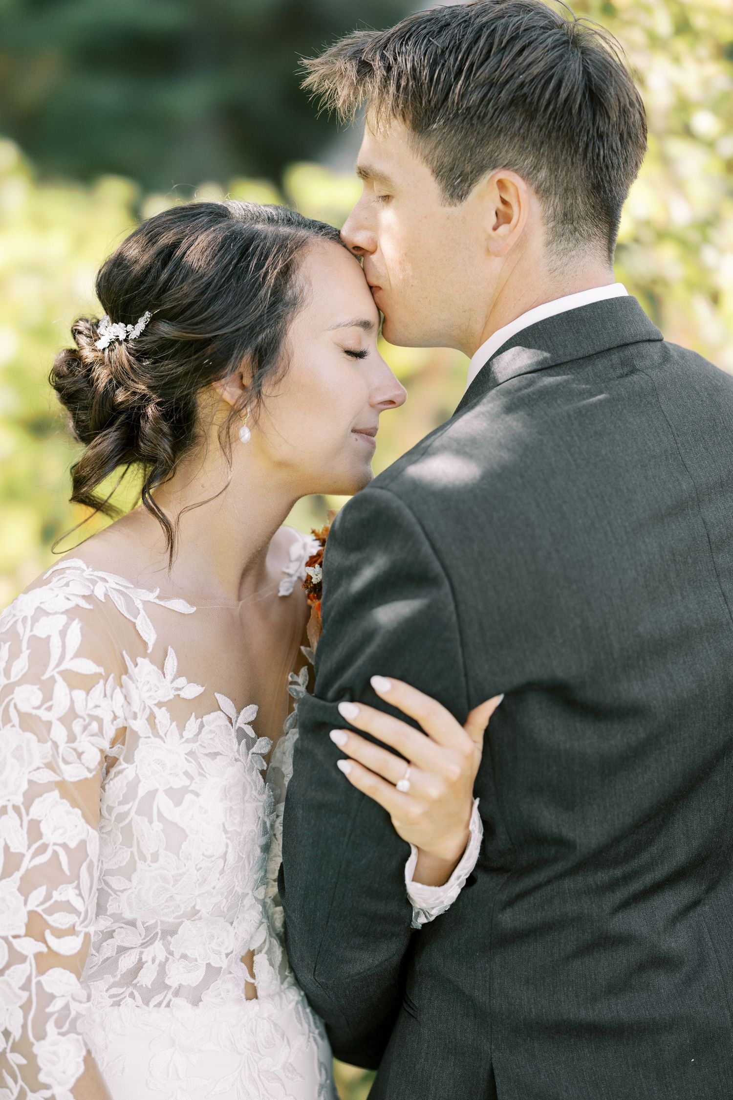 Romantic wedding portrait of a couple embracing outdoors, bride in lace dress and groom in dark suit.