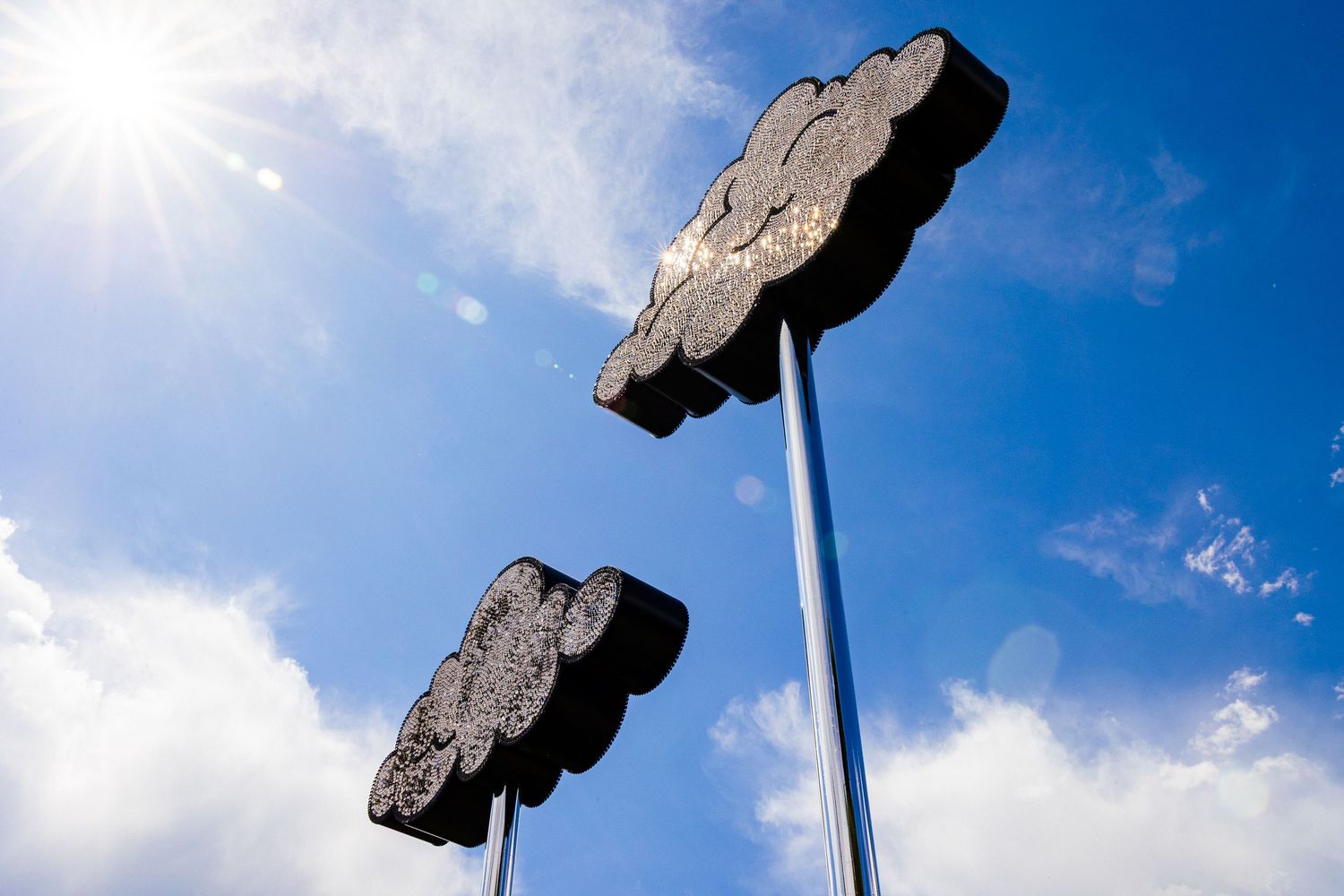 A tall flagpole stands against a bright blue sky with sunburst and scattered white clouds.