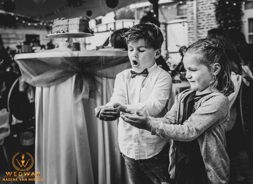 Two children playing handheld video games together at a formal event in black and white photography.