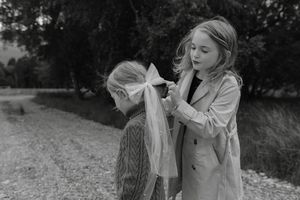 A black and white image shows someone styling hair outdoors in a peaceful natural setting.