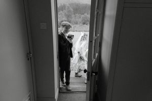 A black and white photograph shows a person walking through a narrow hallway with doorways visible along the walls.
