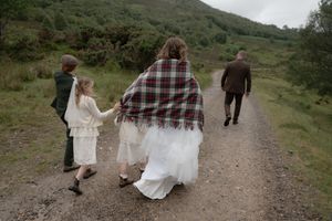 Wedding party walking along a scenic mountain path surrounded by green hills and natural landscape.