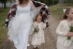 A family in rustic wedding attire walks along a mountain trail holding hands and bouquets.