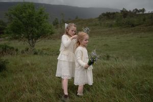 Couple in elegant attire walks through a serene hillside meadow on their wedding day.