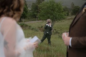 A scenic outdoor wedding ceremony in a grassy meadow with mountains and trees in the background.