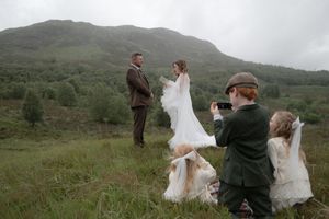 A couple in wedding attire stands on a misty mountainside as the bride's dress billows in the wind.