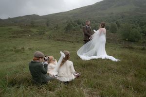 A romantic wedding photoshoot in the Scottish Highlands with rolling green hills and dramatic cloudy skies in the background.
