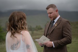 A wedding couple exchanges vows while standing together against a moody mountain backdrop.