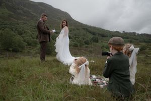 A couple shares an intimate moment during their wedding ceremony in the Scottish highlands on a cloudy day.