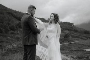 A couple in wedding attire shares an intimate moment against a scenic mountain landscape in black and white.