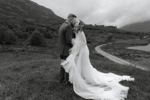 A couple in wedding attire poses against dramatic mountain landscapes in black and white photography.
