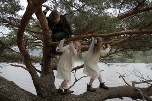 People sitting on tree branches near a lake on a winter day with snow covering the ground.