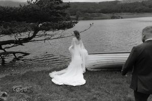 A scenic wedding photoshoot by a lake with rolling hills and trees in the background.