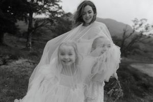 A bride in a flowing white dress and veil stands outdoors against a natural landscape at sunset.