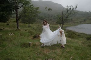 A flowing white dress billows in the wind against a misty mountain landscape beside a serene lake.