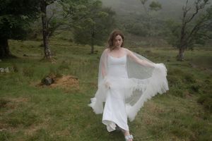 A bride in a flowing white wedding dress twirls gracefully in a scenic outdoor setting with rolling hills in the background.