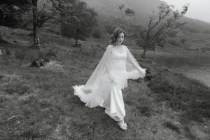 A bride in a flowing white dress and veil twirls gracefully on a misty hillside in black and white photography.