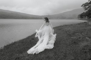 A flowing white wedding dress billows in the wind against a misty mountain lake landscape.