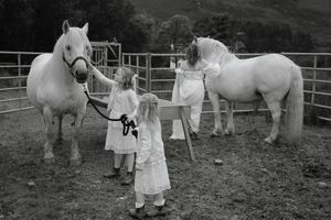 Two white horses stand in a paddock with handlers wearing traditional white clothing in a black and white photograph.