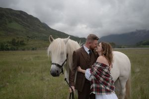 A couple shares a romantic moment with their horses in a misty mountain meadow during an outdoor photoshoot.