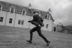 A series of black and white photos showing a person leaping and jumping across a grassy field near buildings.