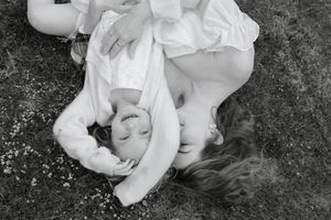 A black and white artistic portrait of someone lying on grass in white clothing.