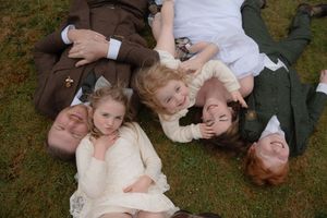 People in formal attire lying on grass in a row creating an artistic wedding photo composition.