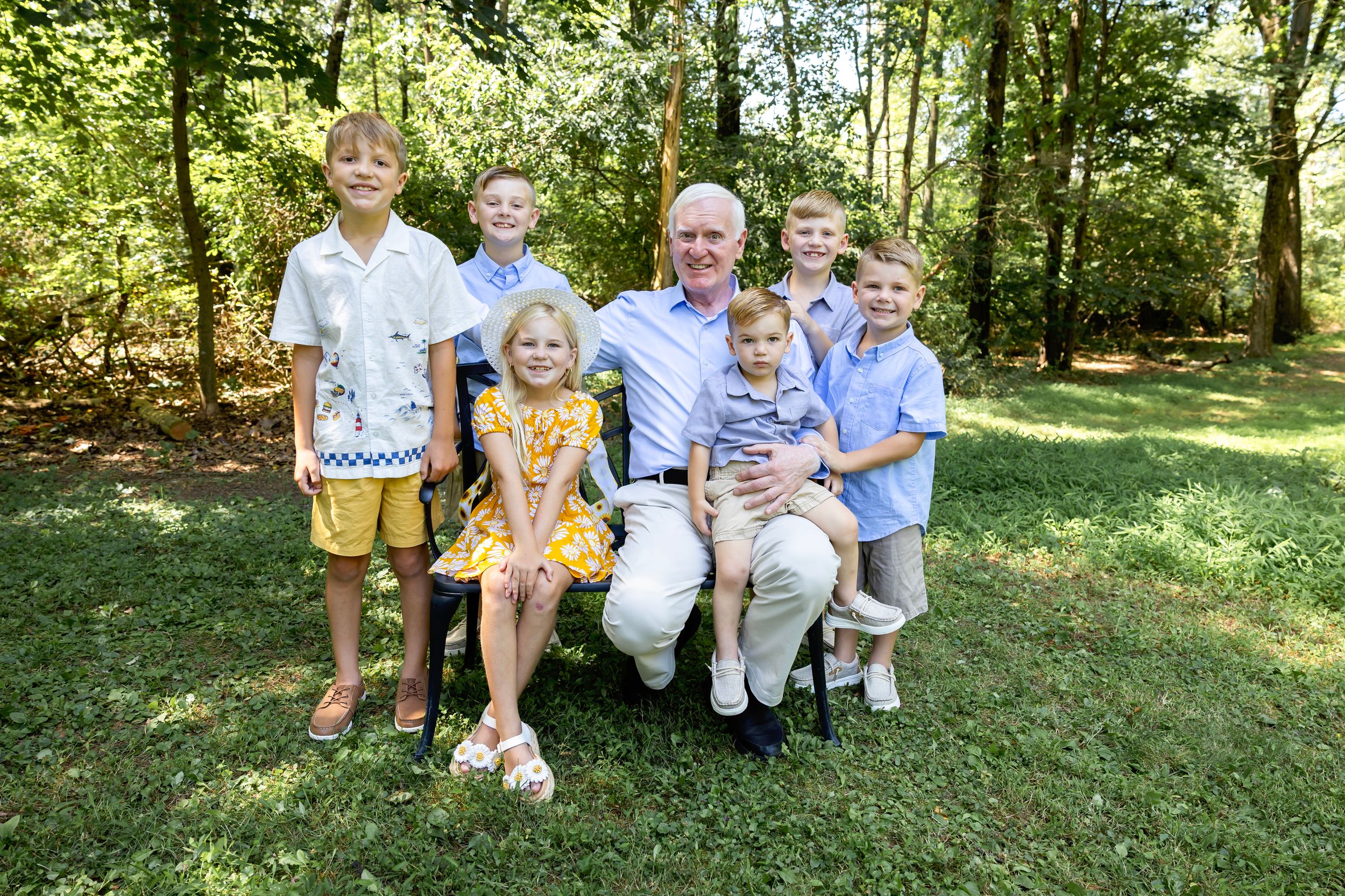 Family group wearing coordinated blue and white outfits poses together on grassy hill in wooded setting.