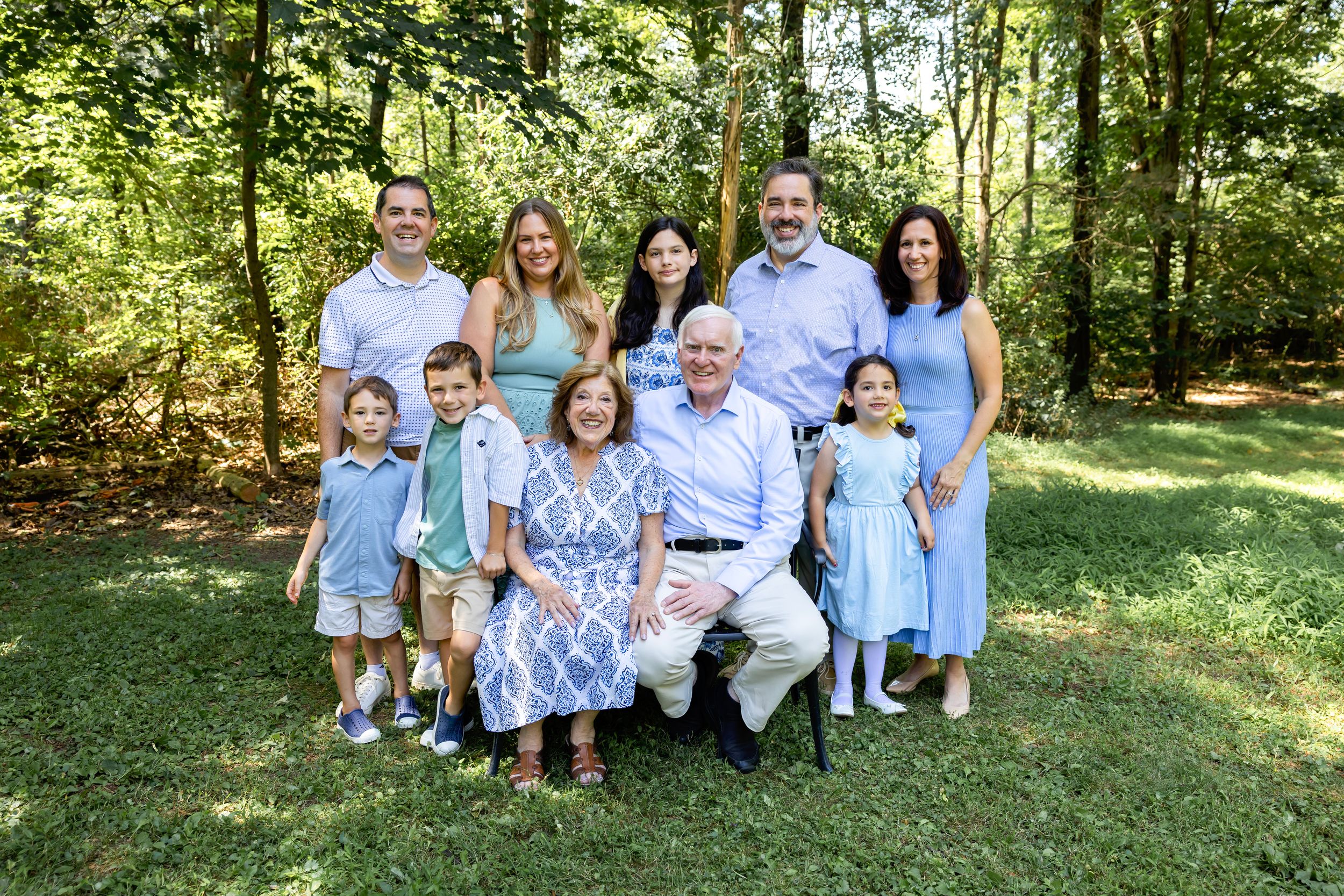 Multi-generational family wearing coordinating blue and white outfits poses together in a sunny outdoor setting.