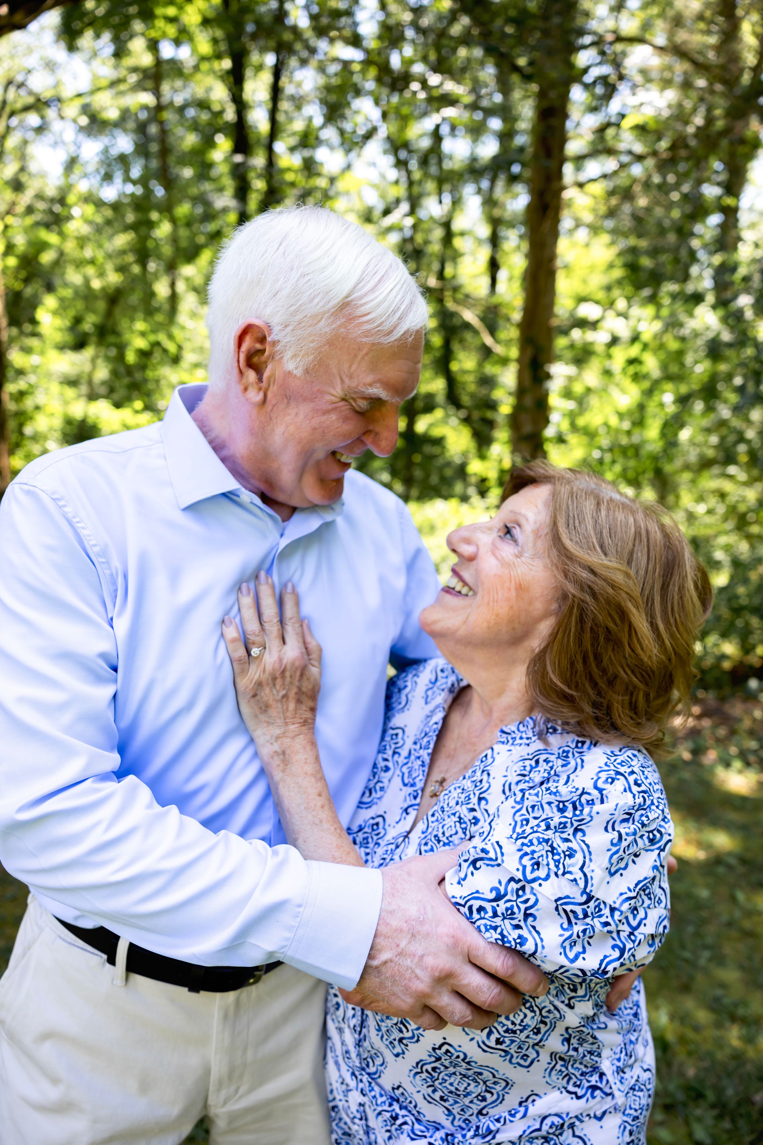 Couple in blue and white outfits share romantic candid moments while laughing together in a wooded setting.