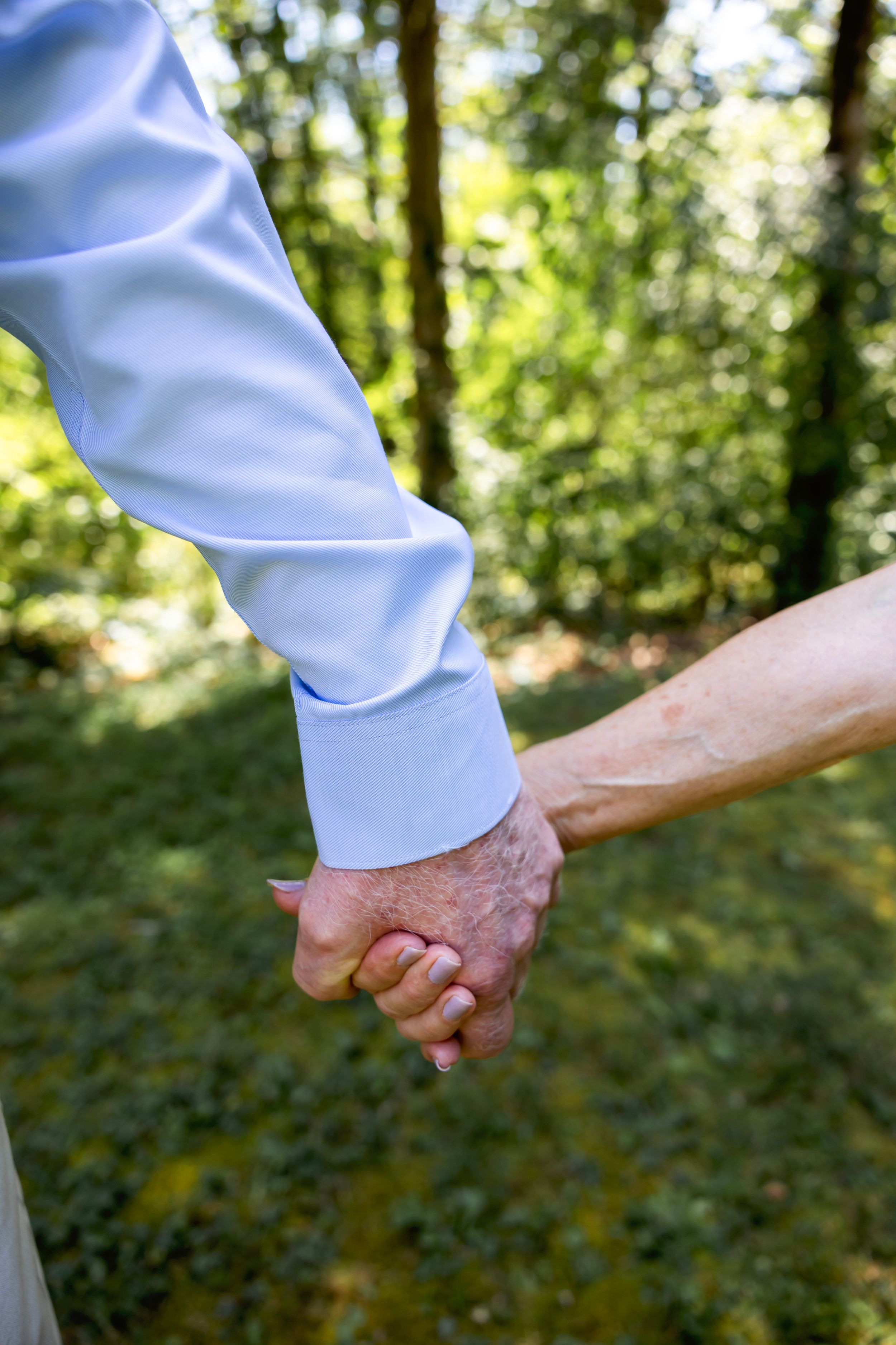 Close-up of hands holding each other against blurred green forest background.