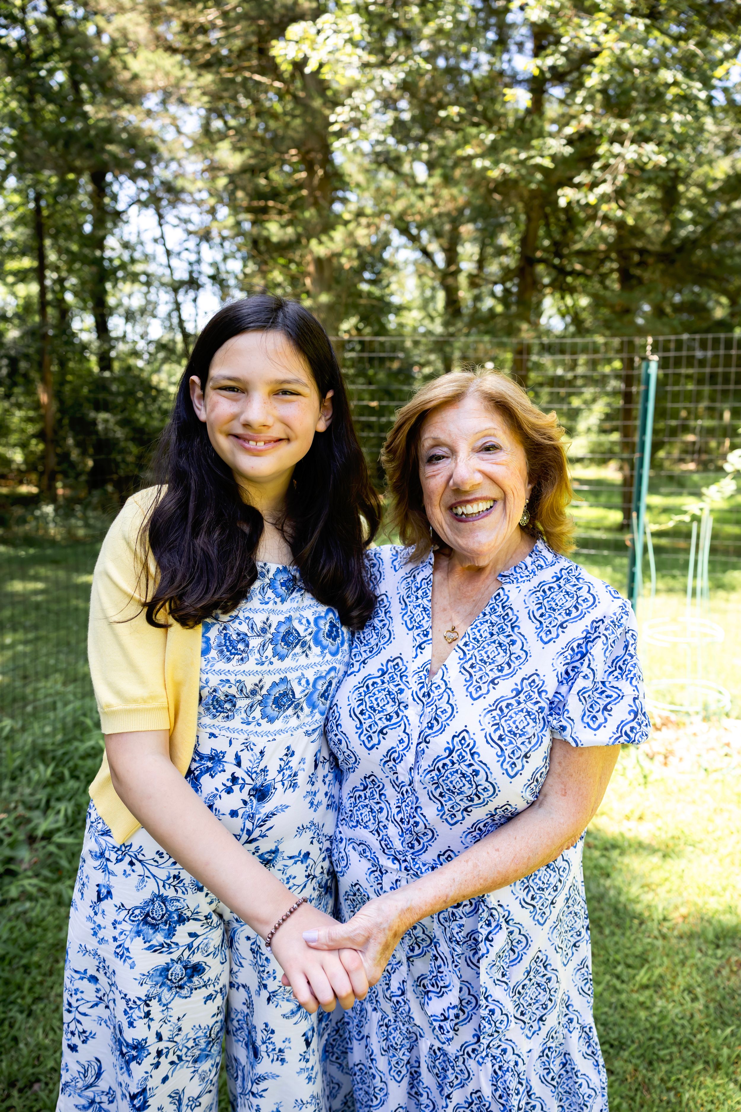 Mother and daughter wearing matching blue and white patterned dresses embrace while smiling outdoors.