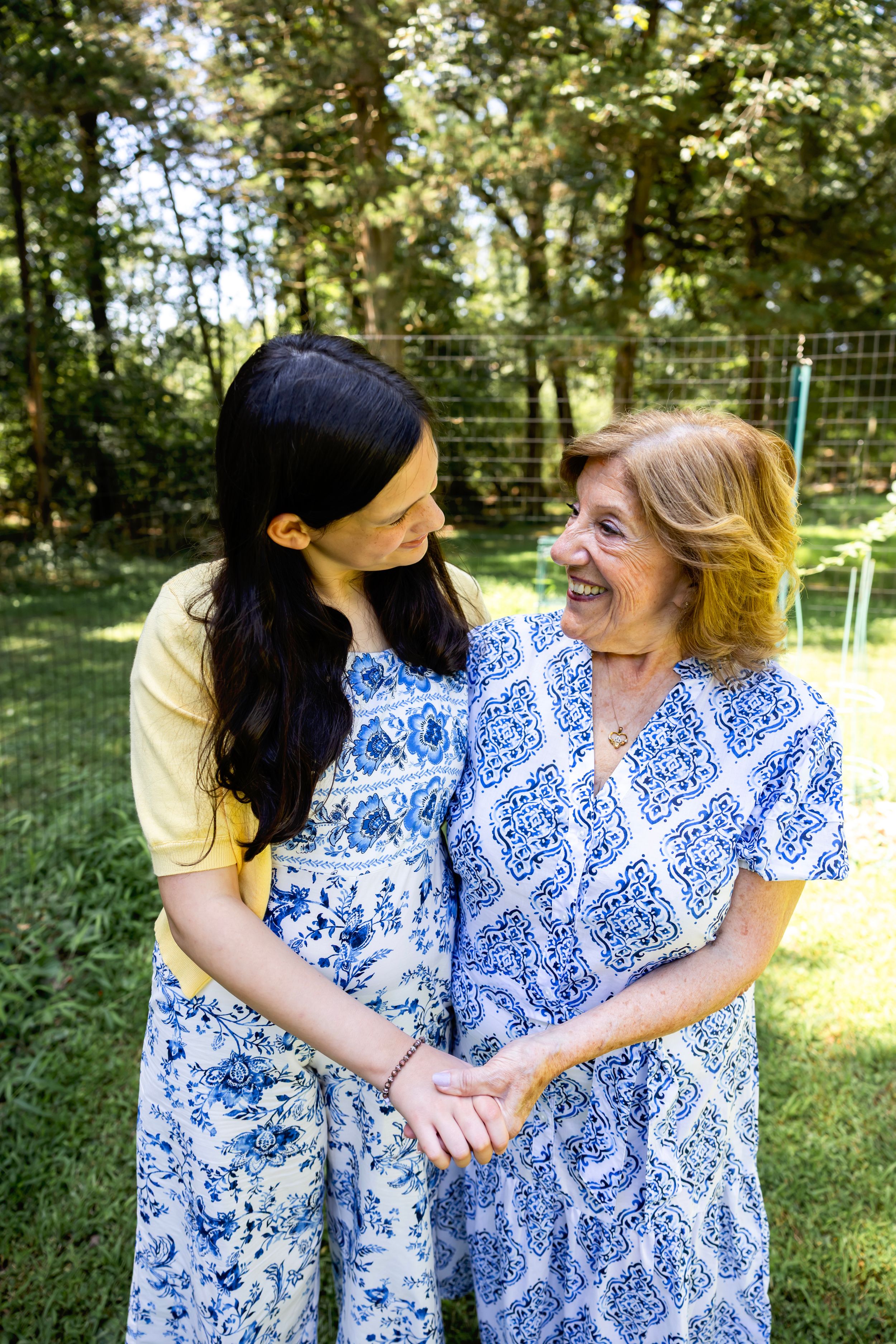 Two people wearing matching blue and white floral dresses share tender moments in a sunny outdoor setting.