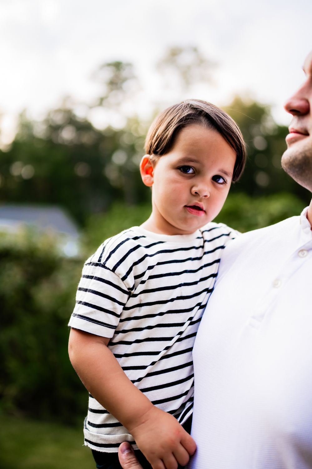 A child in a striped shirt looks up at someone while standing outdoors in natural lighting.
