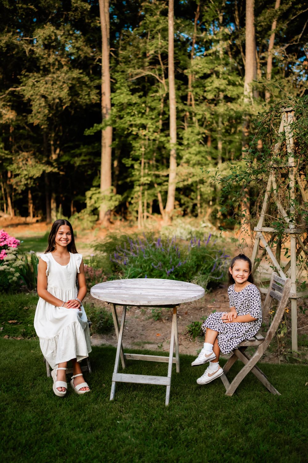 Children sit and play in a wooded outdoor setting with rustic furniture.