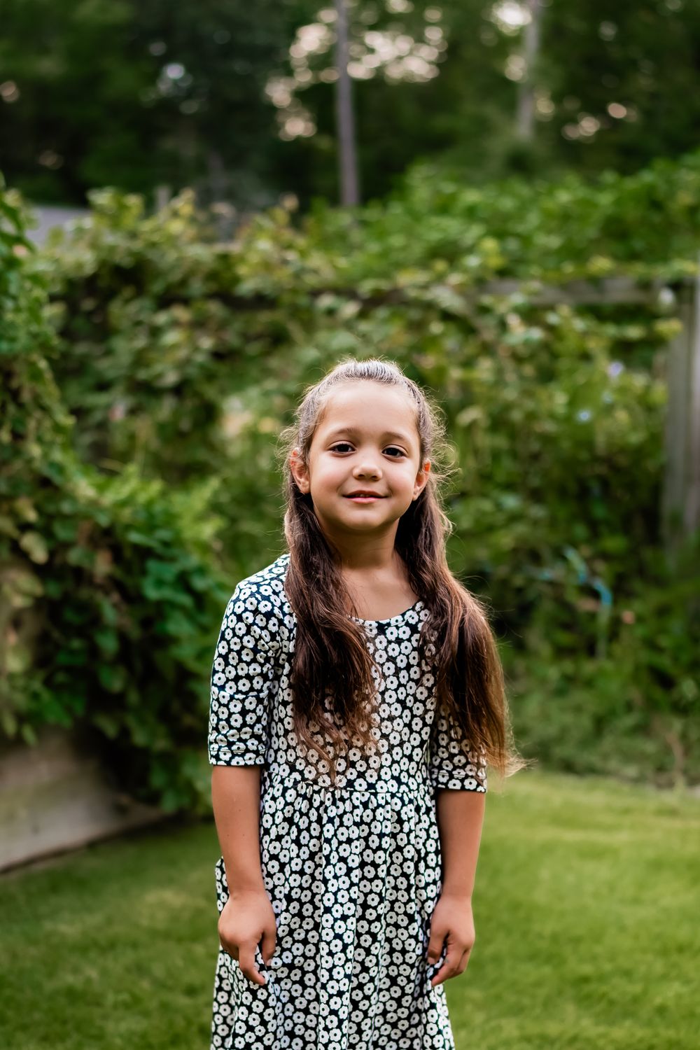 A child in a black and white floral dress plays in a lush green backyard garden setting.