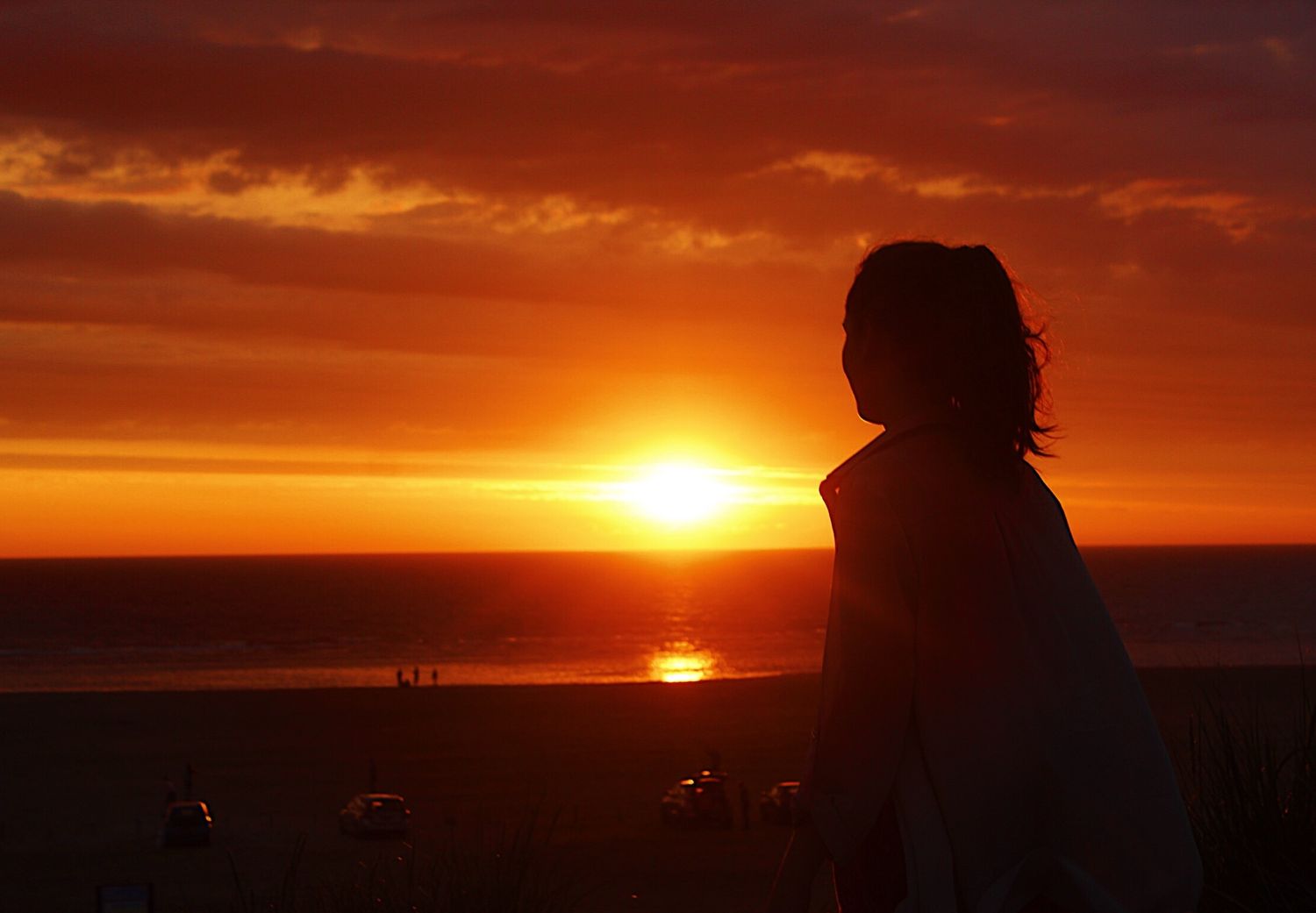 Silhouette of a woman watching a stunning red and orange sunset over the ocean horizon.