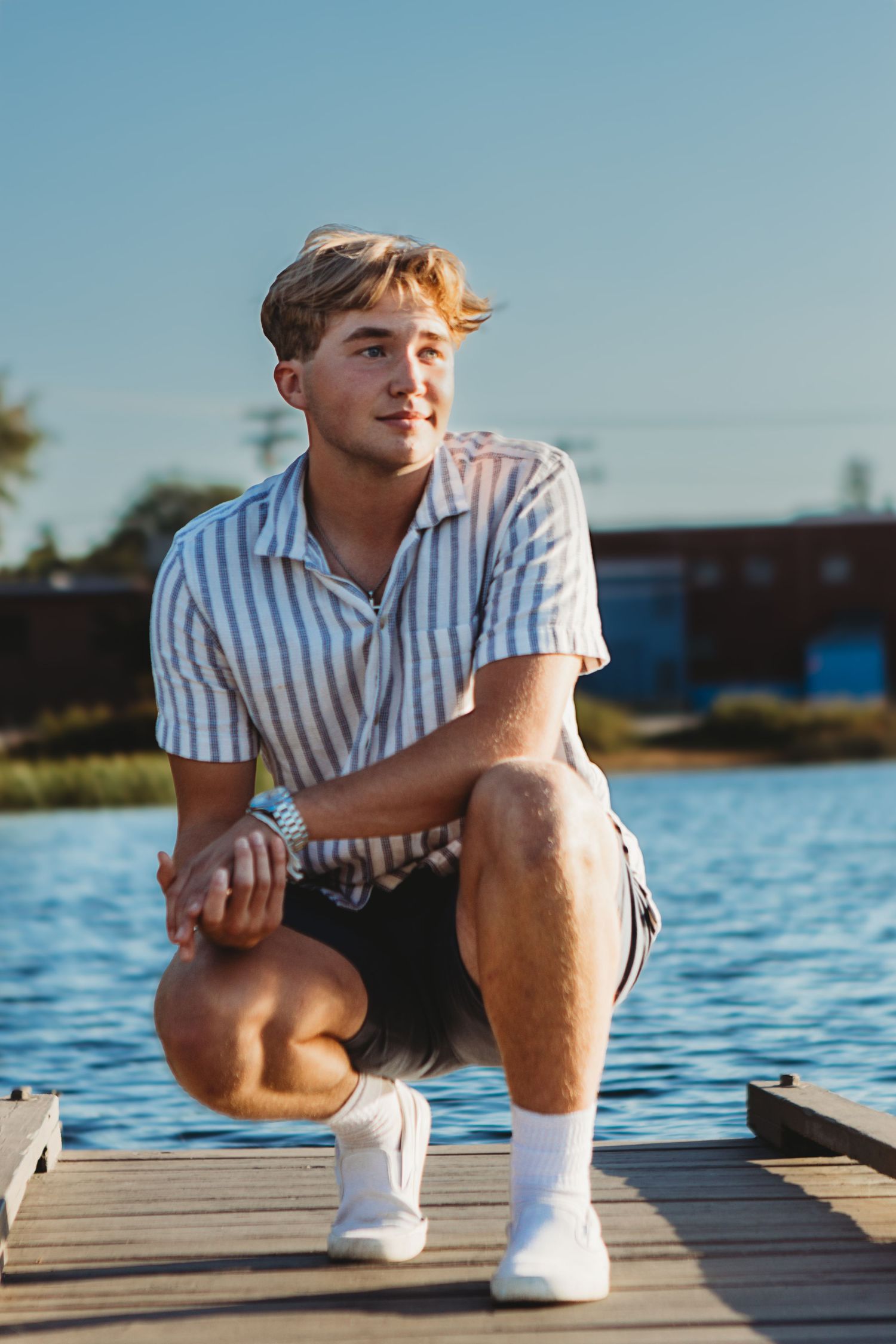 Person in striped shirt sitting on wooden dock by calm water during sunset.