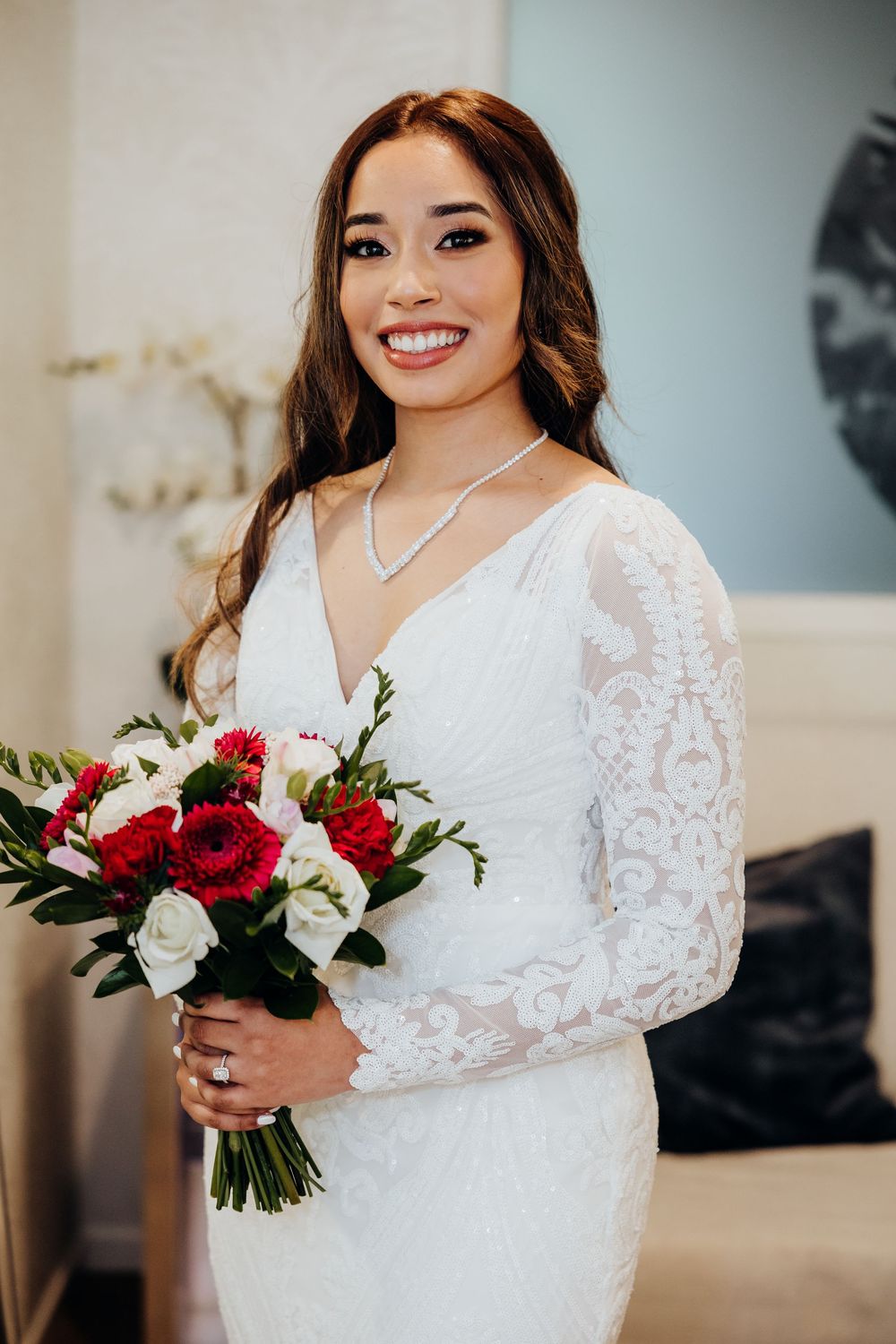 A wedding dress with delicate lace sleeves and a bouquet of red and white flowers.