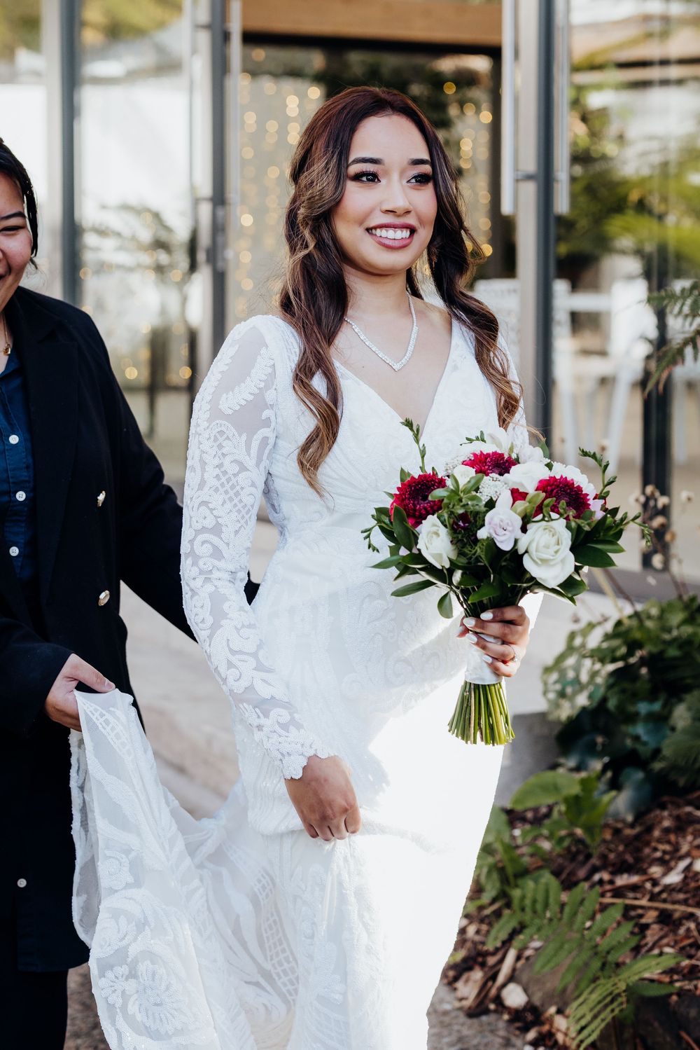 A bride in a white lace gown holds a vibrant bouquet of red and white flowers.