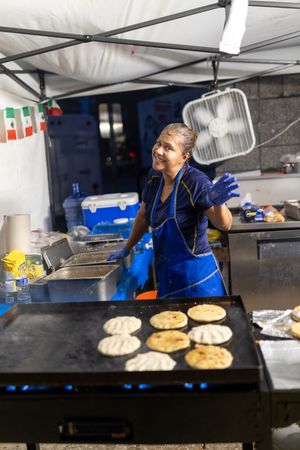 Food vendor cooking flatbreads on a large griddle at an outdoor market stall.