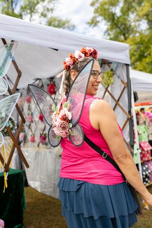 Festival attendee in pink top and blue skirt with floral hair accessories browsing vendor displays.