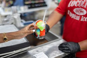 Hands preparing colorful frozen drink at concession stand counter.