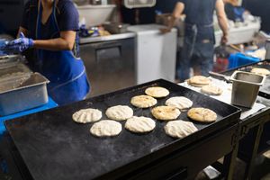 Fresh arepas cooking on a large flat top grill at an outdoor food vendor station.