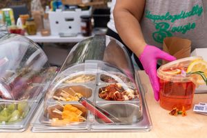 Hands assembling multiple meal prep containers with colorful fresh ingredients and portioned foods on a kitchen counter.