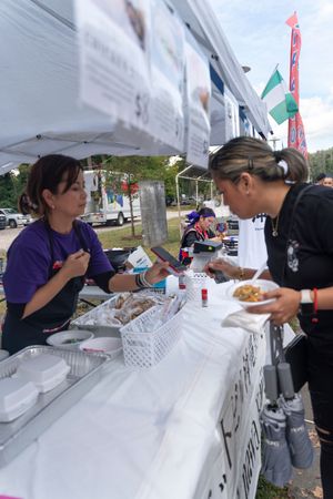 A food vendor booth at an outdoor festival with customers being served at the counter.