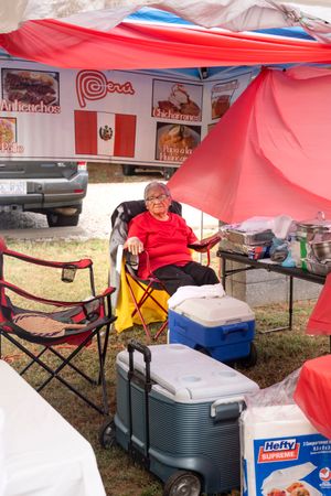 Red canopy tent setup at outdoor event with camping chairs and coolers visible.
